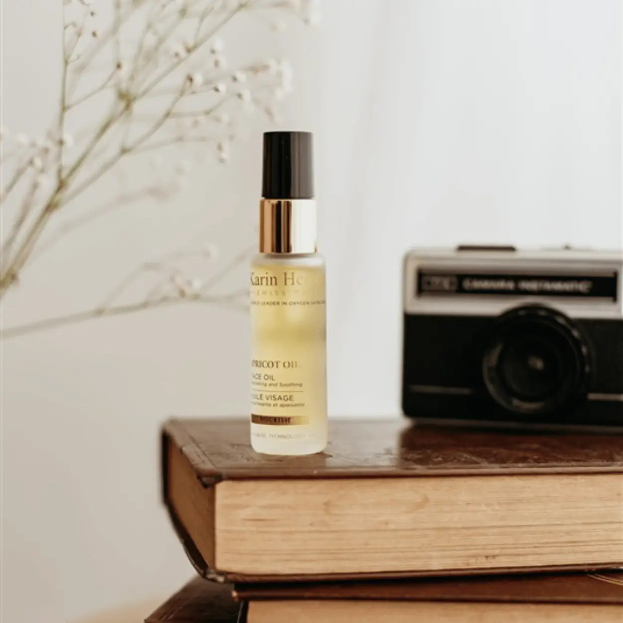 Karin Herzog Apricot Oil bottle displayed on stacked books with a vintage camera in the background.