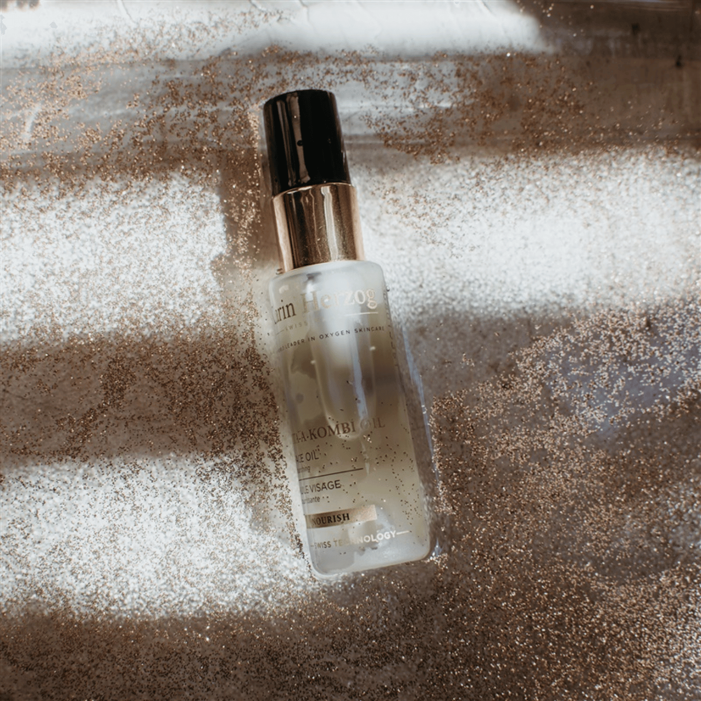 Karin Herzog Vita-A-Kombi Oil bottle resting on a sparkling surface with soft lighting and scattered shimmer, highlighting its luxurious and radiant skincare appeal.