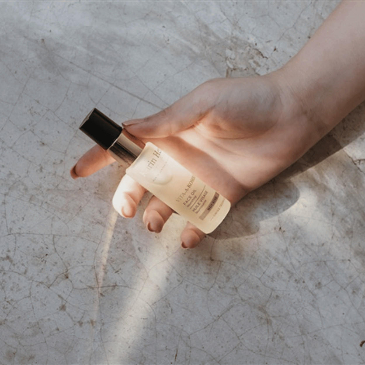 Karin Herzog Vita-A-Kombi Oil held in a sunlit hand, highlighting the product’s golden clarity and luxurious texture in natural light.