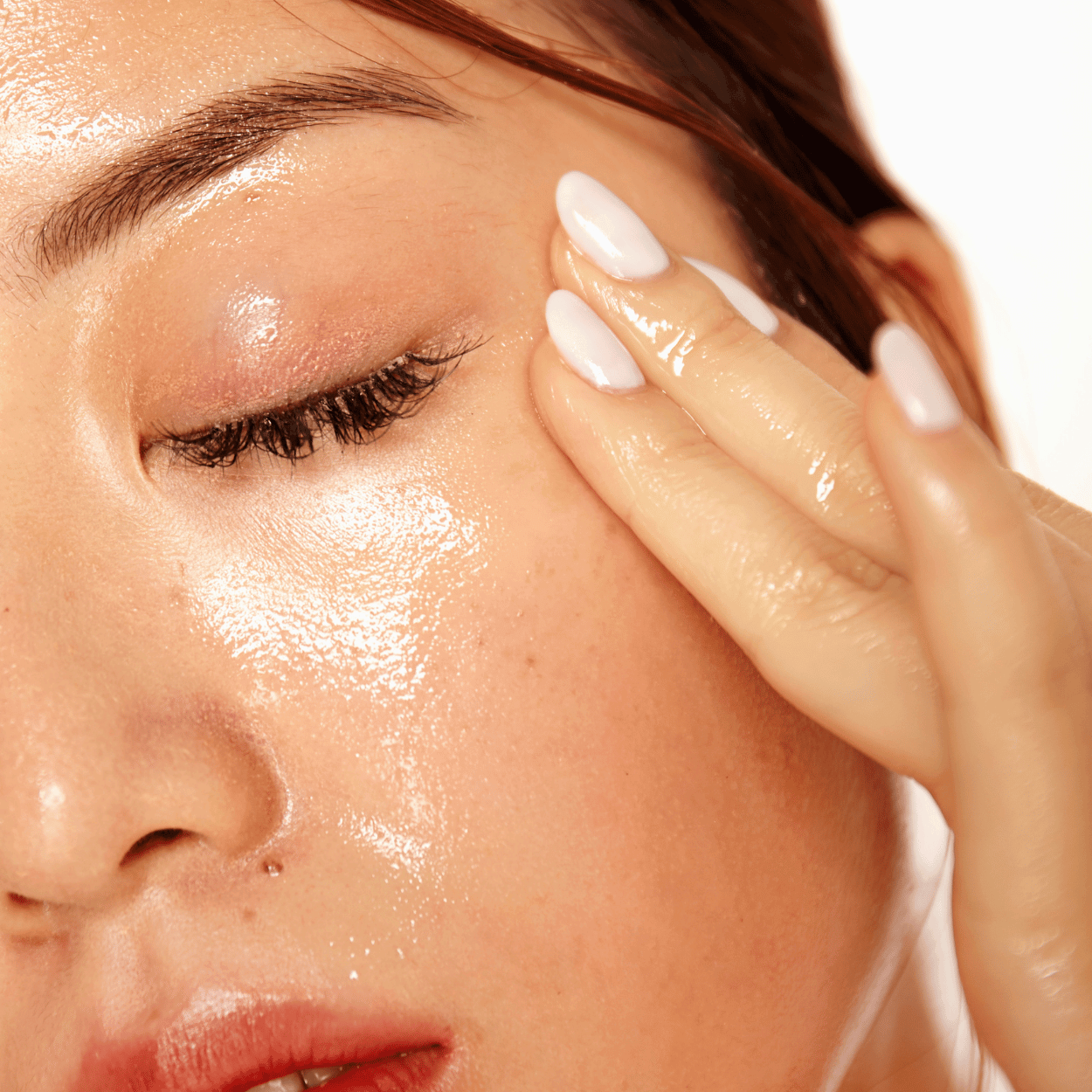 Close-up of a woman applying apricot face oil to her cheek, showcasing radiant and hydrated skin.
