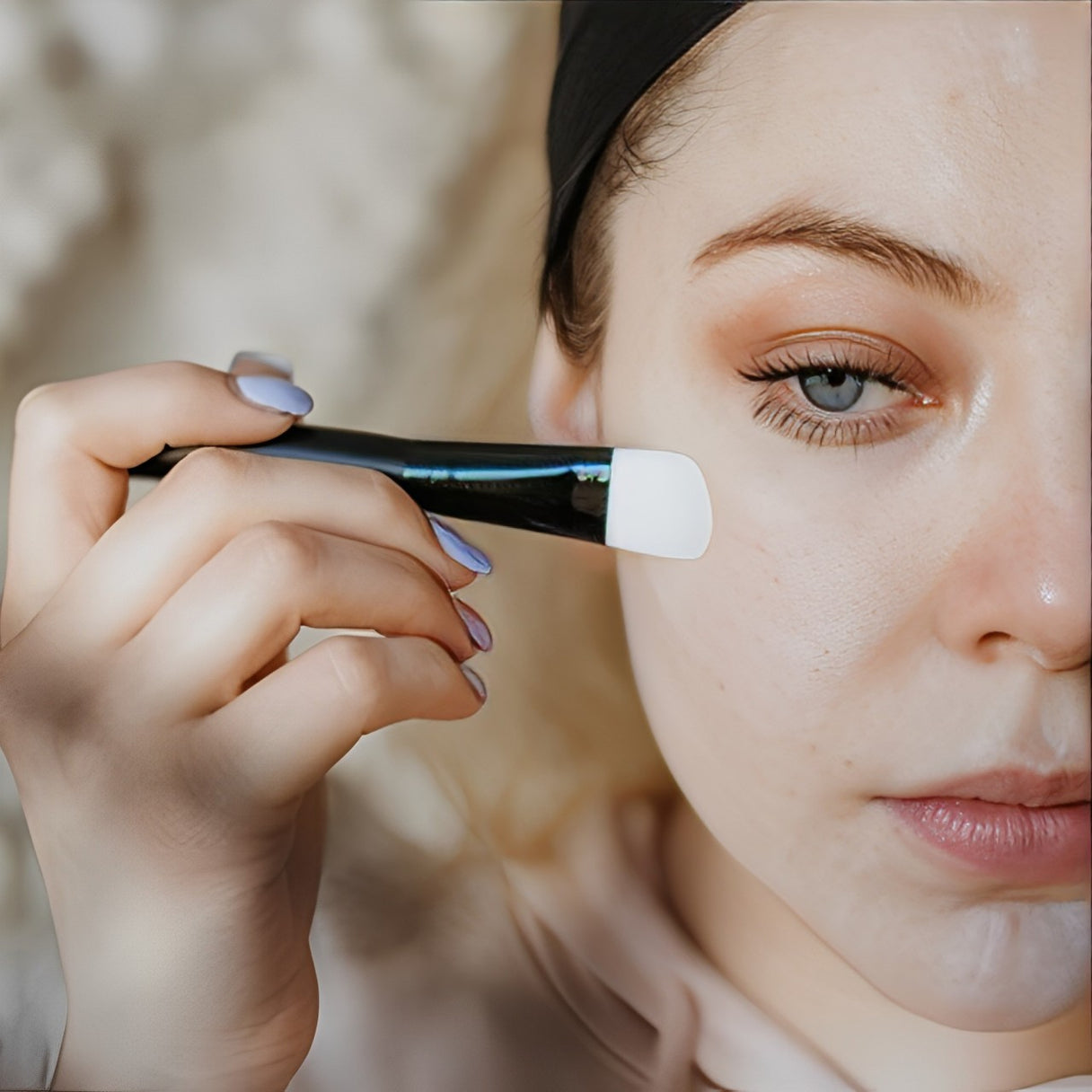 A woman applying a Karin Herzog cream on her face using a face brush, demonstrating a gentle and effective skincare routine.