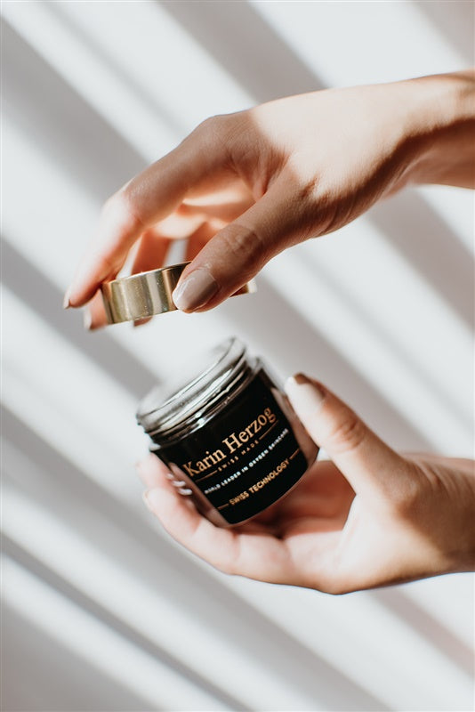 A woman’s hand opening a jar of Karin Herzog anti-ageing cream, highlighting skincare and youthful skin care routine.