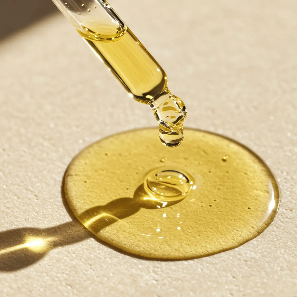 Dropper releasing a drop of apricot oil onto a smooth surface, highlighting its luxurious golden texture.
