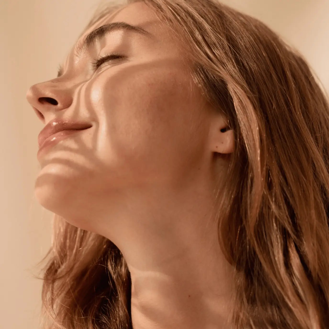 Close-up of a woman with radiant, smooth skin basking in soft sunlight, showcasing the nourishing effects of Karin Herzog facial oils.