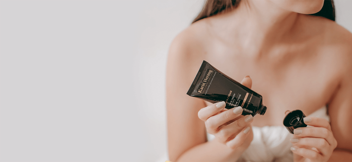 A woman applying Karin Herzog AHA Exfoliation Face Cream, a gentle overnight treatment with mild fruit acids and nourishing vitamins to rejuvenate and transform skin.