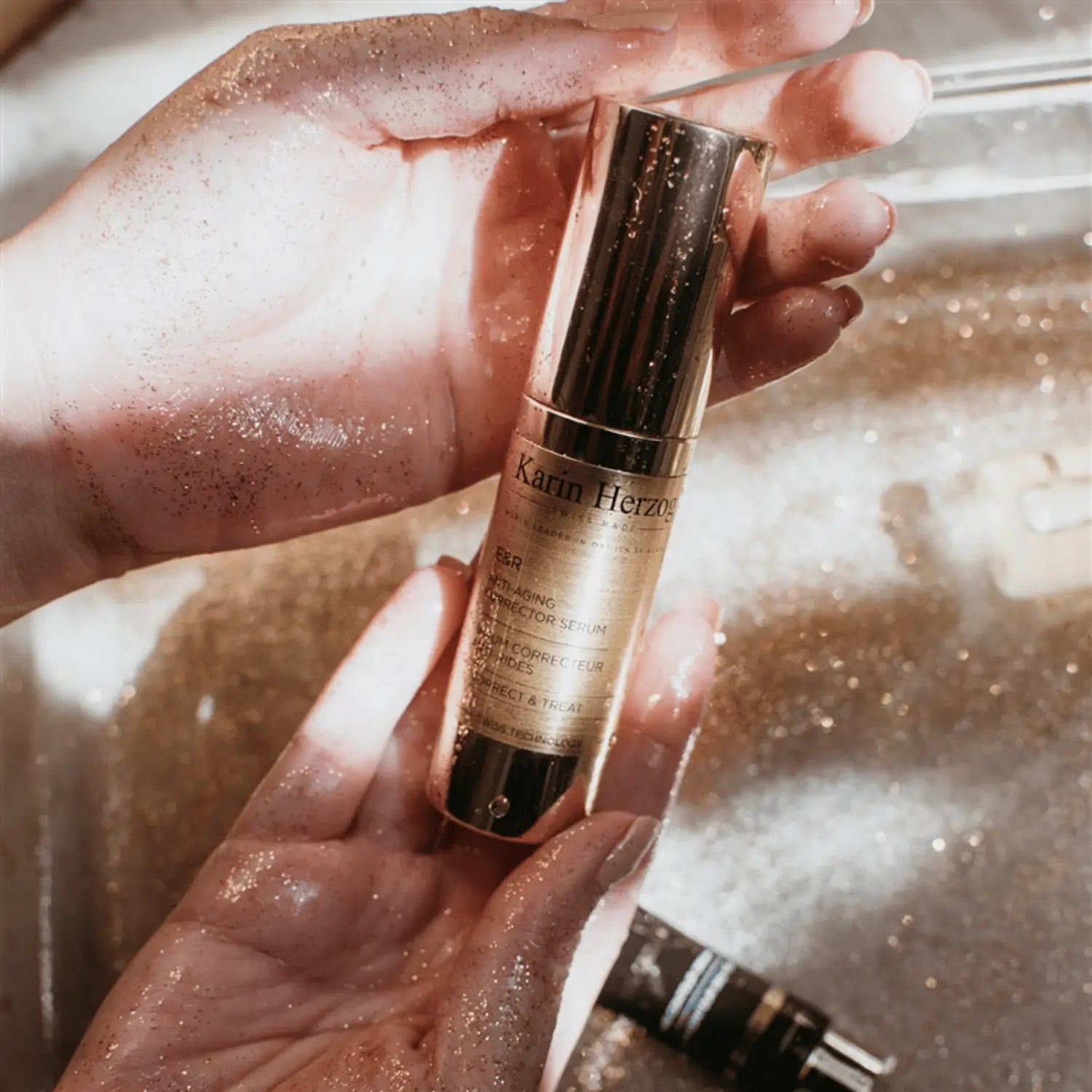 Hands sparkling with golden shimmer holding Karin Herzog’s ER Anti-Aging Skin Corrector Serum, evoking radiance and skin perfection.