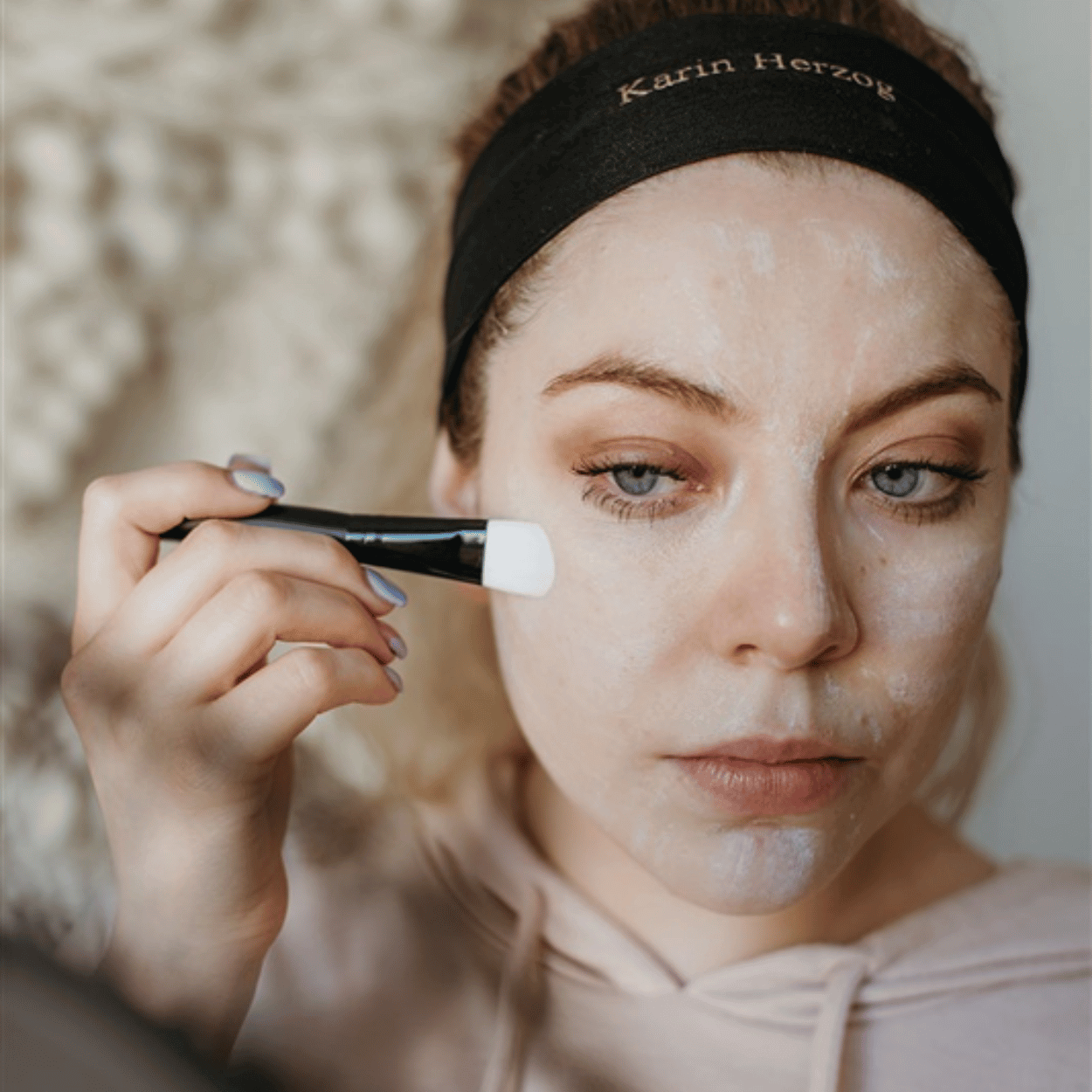 Woman applying Karin Herzog Oxygen Skincare with a face brush, wearing a Karin Herzog headband — part of her hydrating skincare routine.