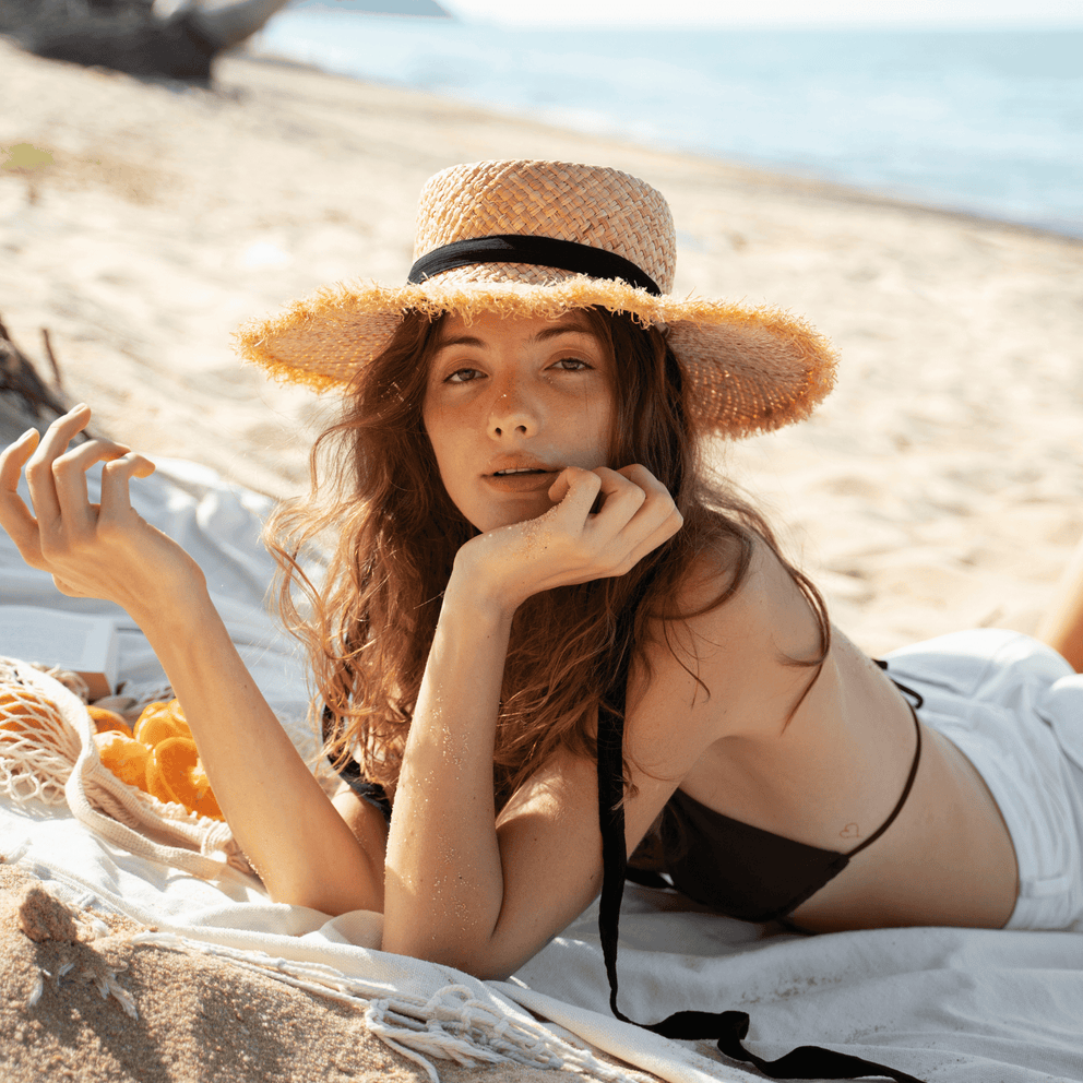 Young woman with glowing skin lounging on the beach in a straw hat, exuding natural radiance and summer freshness — the perfect vibe for Karin Herzog Oxygen Hyalu Lift.
